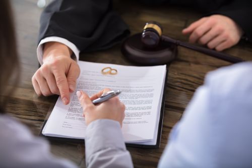 Close-up Of A Female Signing Contract On Desk In Courtroom with wedding bands - Fremstad Law