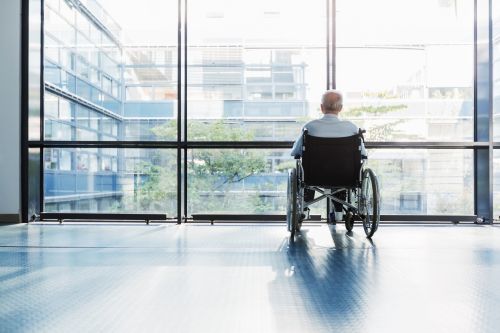 Senior Man in Wheelchair looking out of a window in a hospital corridor. - common signs of nursing home abuse concept