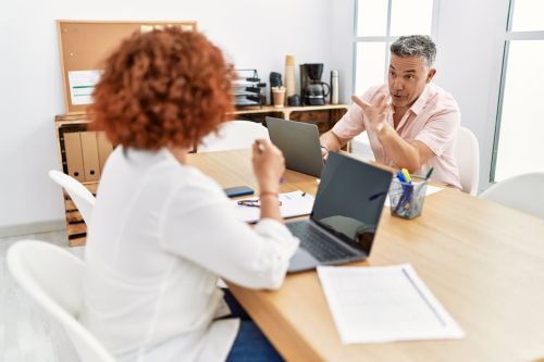 Middle age man and woman business workers using laptop working at office and having a disagreement - shareholders disputes concept